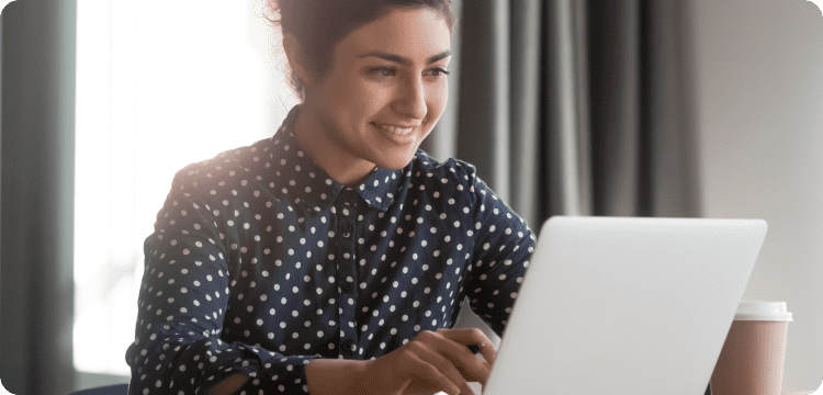 Imagen de una mujer leyendo la pantalla de su computador sonriendo en referencia a las mejores prácticas de las íneas de asunto del correo electrónico
