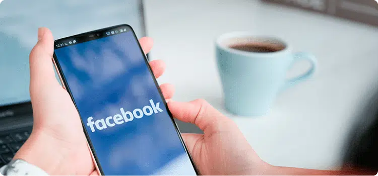 Manos de una persona sosteniendo su celular con la pantalla de inicio de Facebook